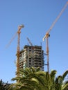 Cranes and under-construction apartment building against blue sky. Royalty Free Stock Photo