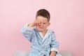 Cranky child boy refuses to go to bed. Kid boy in bathrobe on pink background Royalty Free Stock Photo