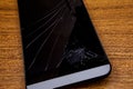 Crashed mobile phone on the table. Black mobile phone on the wooden table with crashed lcd display. Mobile technology concept. Des