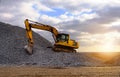 Crawler excavator in the rays of the setting sun at sunset digs earth and sand at a construction site for the construction of the Royalty Free Stock Photo