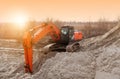 Crawler excavator in the rays of the setting sun at sunset digs earth and sand at a construction site for the construction of the Royalty Free Stock Photo