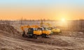 Crawler excavator in the rays of the setting sun at sunset digs earth and sand at a construction site for the construction of the Royalty Free Stock Photo