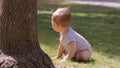 Crawling baby boy backs away from a tree and turns to go investigate something else across the grass