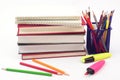 Crayon or colored pencils in box with side stack of books and school supplies on white background. Royalty Free Stock Photo