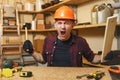 Handsome smiling young man working in carpentry workshop at wooden table place with piece of wood