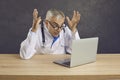 Crazy angry senior male doctor screaming in frustration looking at laptop screen.