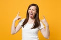 Crazy blinking young woman in white casual clothes depicting heavy metal rock sign, horns up gesture showing tongue