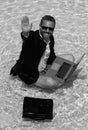 Crazy business man in a business suit works for a laptop standing in the water in pool. Remote work. Crazy freelancer