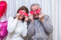 Crazy couple seniors celebrate Valentine's Day. Man and woman cover eyes with red valentine cards and smile. Romantic