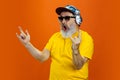 Senior hipster man using devices, gadgets on orange background. Tech and joyful elderly lifestyle concept