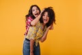 Crazy emotional girls are dabbling and having fun on orange background. Woman laughs and plays hair