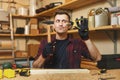 Handsome smiling young man working in carpentry workshop at wooden table place with piece of wood Royalty Free Stock Photo