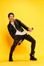 Punk young guy with baseball bit like playing guitar and smiling at camera over yellow background. Concept of music