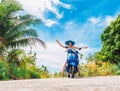 Crazy funny woman with flying hair riding a motorbike on a blue sky and green tropics background. Young girl with dark