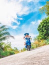 Crazy funny woman with flying hair riding a motorbike on a blue sky and green tropics background. Young bizarre girl Royalty Free Stock Photo