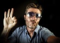 Crazy happy and funny guy with sunglasses and modern hipster look taking selfie self portrait picture with mobile phone camera smi