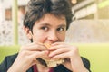 Crazy hungry boy eating double cheeseburger opens his mouth wide and bulges his eyes. The concept of food and unhealthy lifestyle.