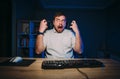 Crazy man with a beard works at night on the computer then gets emotionally angry, makes a funny face. Emotional freelancer gets Royalty Free Stock Photo