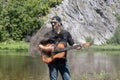 crazy man musician, guitarist on vacation. 23 year guy with beard in black shirt, cap, sunglasses holds steaming guitar