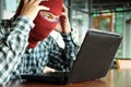 Crazy masked hacker wearing a balaclava touching on head between stealing data from laptop. Internet crime concept.
