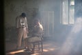 A crazy man in a straitjacket is tied to a chair in an abandoned old clinic and the other insane man coming closer with