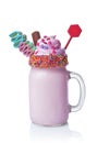Crazy milk shake with pink whipped cream, chocolate bar and colored candy in glass jar