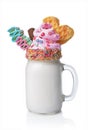 Crazy milk shake with pink whipped cream, chocolate bar, waffle and colored candy in glass jar