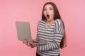 Crazy online study course! Portrait of amazed, surprised woman in striped sweatshirt holding laptop and looking shocked Royalty Free Stock Photo