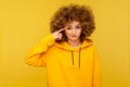 This is crazy! Portrait of curly-haired woman in urban style hoodie making stupid sign with finger near head