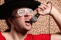 Crazy rock and roller singer with a big black hat, party glasses in front of a cheetah skin background