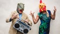 Crazy senior couple dancing at carnival party wearing t-rex and chicken mask - Old trendy people having fun listening music with