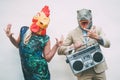 Crazy senior couple wearing chicken and t-rex mask while dancing outdoor - Mature trendy people having fun celebrating