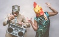 Crazy senior couple wearing chicken and t-rex mask while dancing outdoor - Mature trendy people having fun celebrating