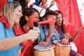 Crazy sport fans playing drums and screaming while supporting their team - Main focus on left girl face Royalty Free Stock Photo