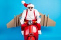 Crazy stylish modern white grey hair bearded santa claus with craft wings drive scooter hurry x-mas party wear red Royalty Free Stock Photo