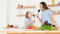 Young mother with happy young little daughter singing in karaoke holding kitchen spoon in hands Royalty Free Stock Photo