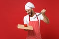 Crazy young male chef cook or baker man in striped apron toque chefs hat posing isolated on red background. Cooking food Royalty Free Stock Photo