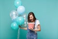 Crazy young woman keeping mouth wide open, holding bucket of popcorn and celebrating with colorful air balloons isolated