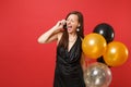 Crazy young woman in little black dress holding air balloons, talking on mobile phone, screaming isolated on red Royalty Free Stock Photo