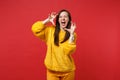 Crazy young woman in yellow fur sweater shouting, growling like animal, making cat claws gesture isolated on red Royalty Free Stock Photo