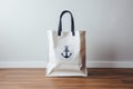 Cream beach tote bag with nautical themes on wooden and white wall background, empty space