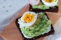 Cream cheese avocado toast with soft boiled egg, microgreen of garden cress and sesame mix on wooden board on white