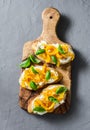 Cream cheese, roasted yellow bell pepper, basil bruschetta on cutting board on grey background