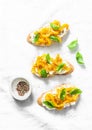 Cream cheese, roasted yellow bell pepper, basil bruschetta on on light background, top view. Copy space