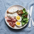 Cream cheese sandwiches, boiled egg, prosciutto, spinach, tomatoes - delicious healthy breakfast, snack, tapas on blue background Royalty Free Stock Photo