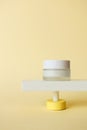 Cream facial moisturizer cream standing on abstract pedestal on pastel yellow background with copy space, front view