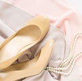 Cream heeled women`s shoes, pink dress and pearls necklace on white background. Royalty Free Stock Photo
