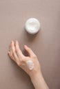 Cream moisturizer smudge apply on woman hand with nude pink manicure on nails and body lotion in glass jar on beige background