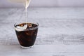 Cream poured in glass with coffee and ice cubes on wodden table.