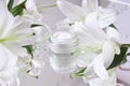 Cream for skin care, natural cosmetics made of flowers and petals. A glass jar of white cream stands among the lily flowers Royalty Free Stock Photo